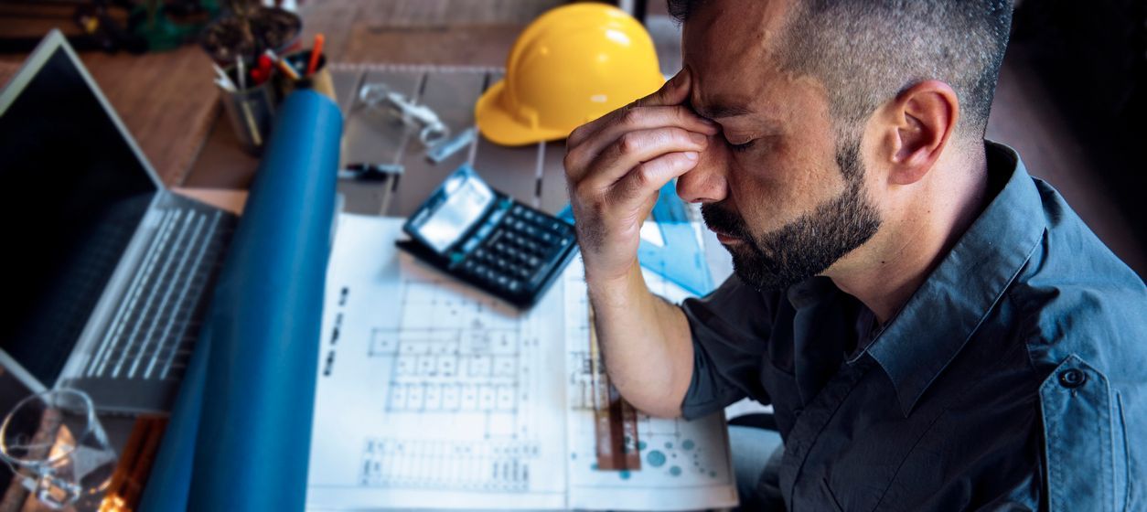 Overworked stressed construction worker frustrated as he looks at blueprints