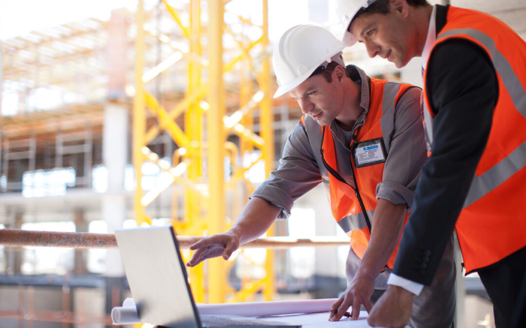 Two construction workers in vests leaning over a laptop looking at the best softwares for small construction companies