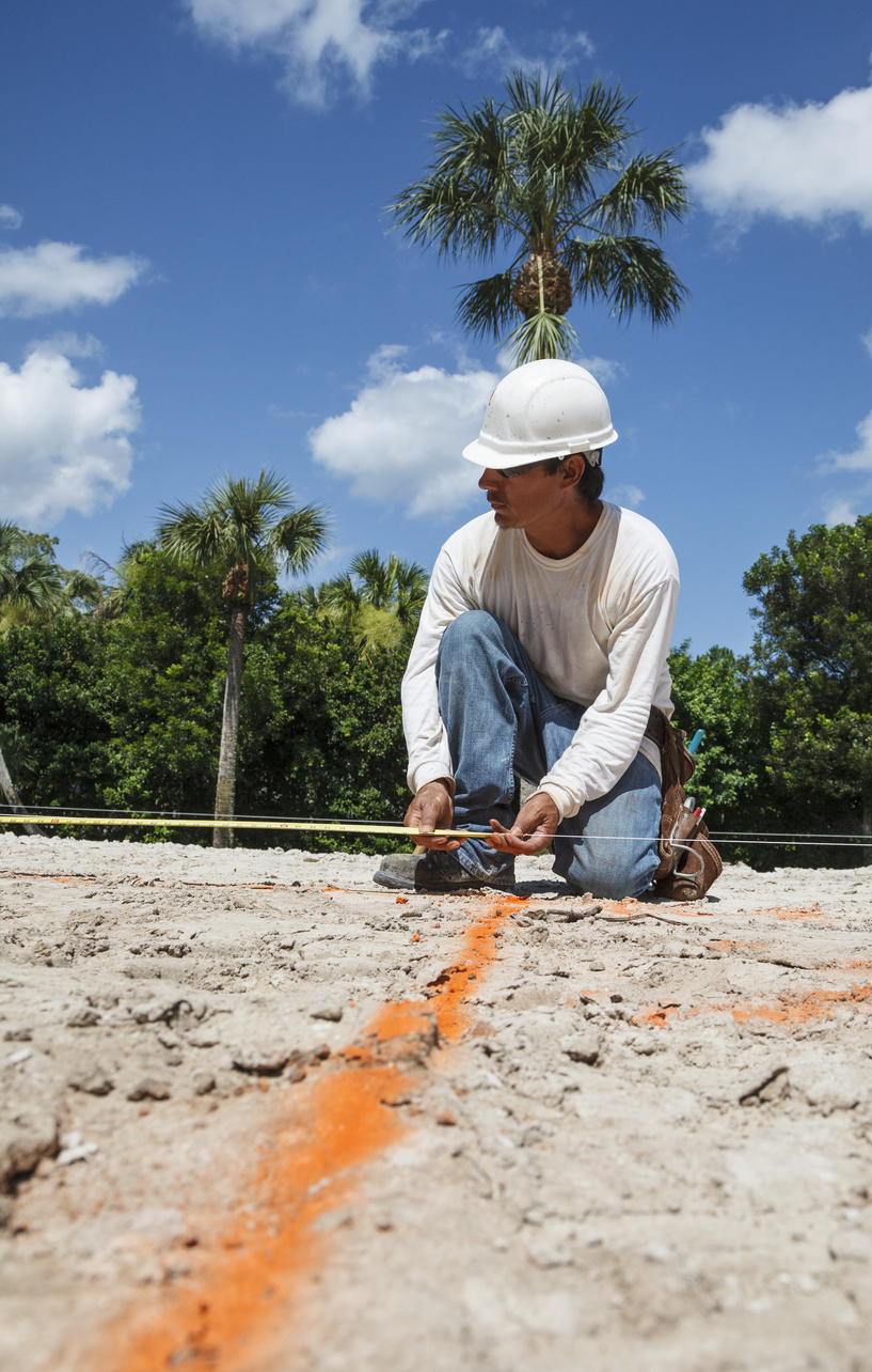 Hispanic construction worker measures off a job site