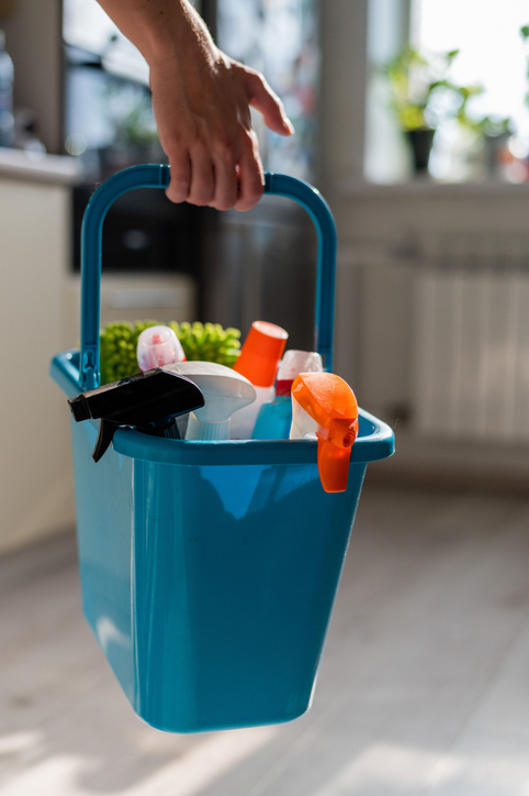 House cleaning concept. Faceless woman holds cleaning products in a blue basket. Closeup of the hands of a female workers house.